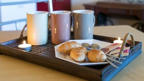A tray with croissants, a candle, and a basket of books on a wooden table. - Villa Iveta- Triple Room (Ground Floor) - Martina (Dubrovnik)