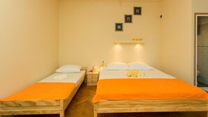 A small, cozy room with two single beds, each with an orange blanket. There is a nightstand with a lamp between the beds, and a shelf above the beds holding a few items. - Villa Iveta- Triple Room (Ground Floor) - Martina (Dubrovnik)