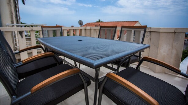 Ein Balkon mit Tisch und vier Stühlen, mit Blick auf eine Wohngegend mit roten Ziegeldächern.
