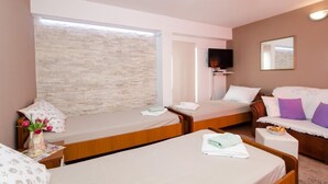 Une chambre d’hôtel avec deux lits simples, un canapé et un téléviseur, ainsi qu’un autre téléviseur fixé au mur.