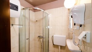 Une salle de bain avec une douche à parois de verre, des toilettes et un sèche-cheveux fixé au mur.