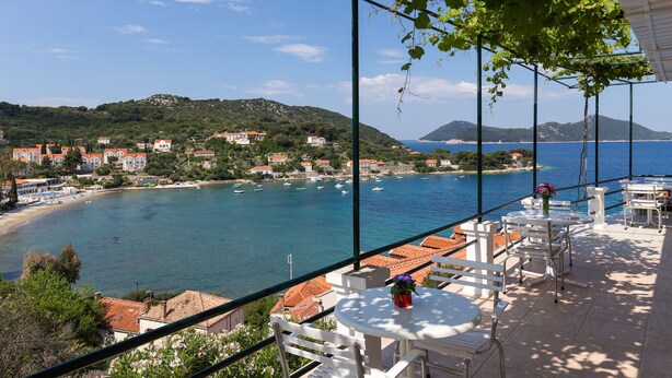 A balcony with white chairs and tables, overlooking a coastal town with buildings and boats. - Apartments Miskovic - Studio Apartment with Balcony and Sea View (East) (Kolocep)