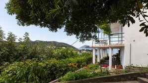 A modern building with a white exterior, surrounded by lush greenery and a view of distant hills. - Apartments Miskovic - Studio Apartment with Balcony and Sea View (East) (Kolocep)