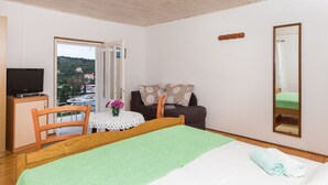A bedroom with a bed, a wooden chair, a small table with a vase of flowers, a television on a cabinet, and a window with a view of buildings. - Apartments Miskovic - Studio Apartment with Balcony and Sea View (East) (Kolocep)