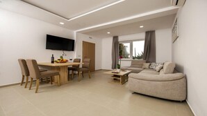 Een moderne woonkamer met een bank, een eettafel met stoelen, een wandgemonteerde flatscreen-tv en een raam met gordijnen.