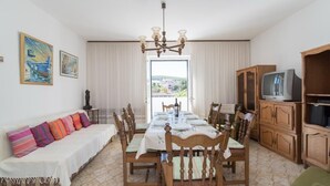 A dining area with a table set for four, wooden chairs, a chandelier, and a television on a wooden cabinet. - Apartment M&P - Four Bedroom Apartment with Terrace Sea View (Supetar)