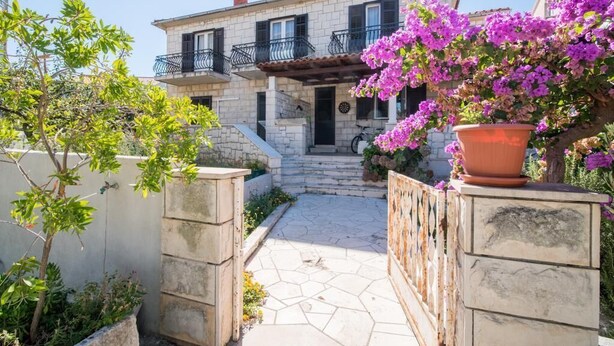 A stone house with a tiled patio, a balcony with black railings, and a potted plant with purple flowers. - Apartment M&P - Four Bedroom Apartment with Terrace Sea View (Supetar)
