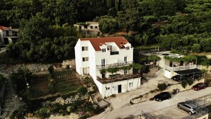 Un bâtiment blanc à deux étages, doté d’un toit recouvert de tuiles rouges, d’un balcon et d’un petit jardin.