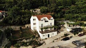 A white two-story building with a red-tiled roof, a balcony, and a small garden area.