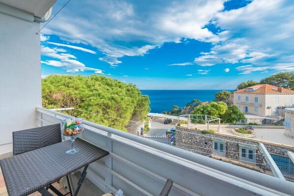 Un balcon donnant sur la mer, une table avec un verre, et un bâtiment en arrière-plan.