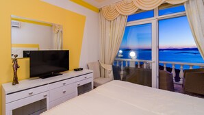 Habitación de hotel con cama, televisor, cómoda y balcón con vista al mar.