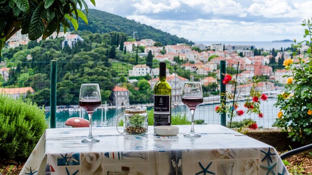 Uma mesa com uma garrafa de vinho, dois copos e um pequeno pote de azeitonas, com vista para uma paisagem costeira.