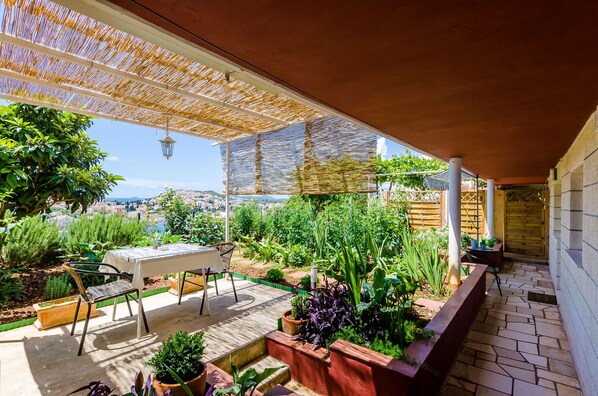 An outdoor patio with a table and chairs, surrounded by potted plants and a view of the city.
