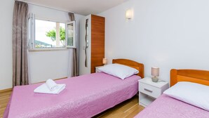 Quarto de hotel com duas camas, janela com cortinas, parede de painéis de madeira e mesa de cabeceira com abajur.
