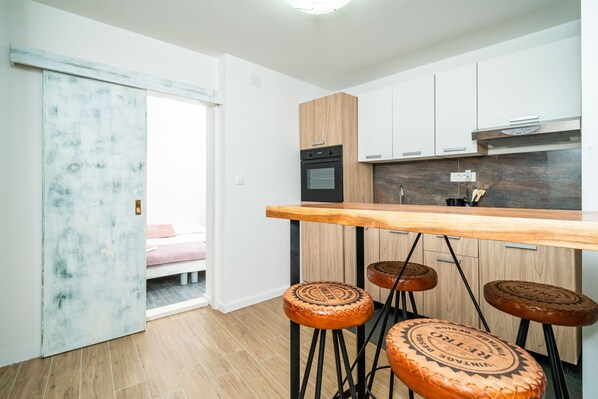 Une cuisine moderne avec des meubles en bois, un four noir et un bar en bois avec des tabourets.