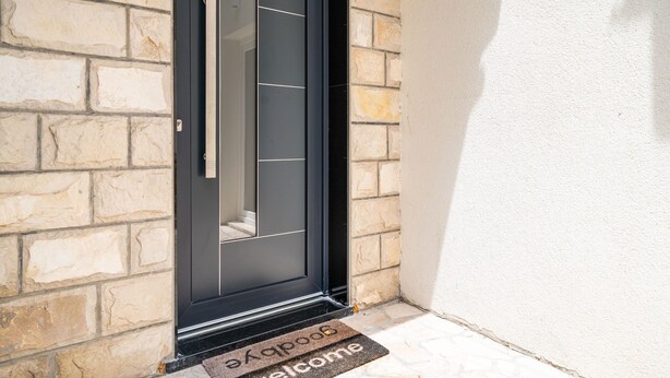 Una puerta negra con felpudo y panel de vidrio.