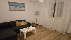 Un salon avec un canapé foncé, une table basse blanche, une lampe et un tableau accroché au mur.
