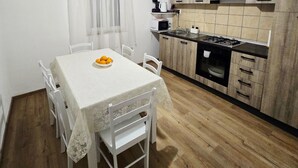 Une table à manger avec des chaises, un saladier rempli de fruits, une cuisine équipée d’une cuisinière, d’un four et de placards.