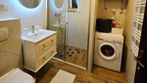 Une petite salle de bain comprenant des toilettes, un lavabo, une douche et un lave-linge.