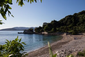 A coastal landscape with a rocky beach, clear blue water, and a building on a hillside. - Villa Dubravka - Superior Studio Apartment with Balcony and Sea View (Mlini)