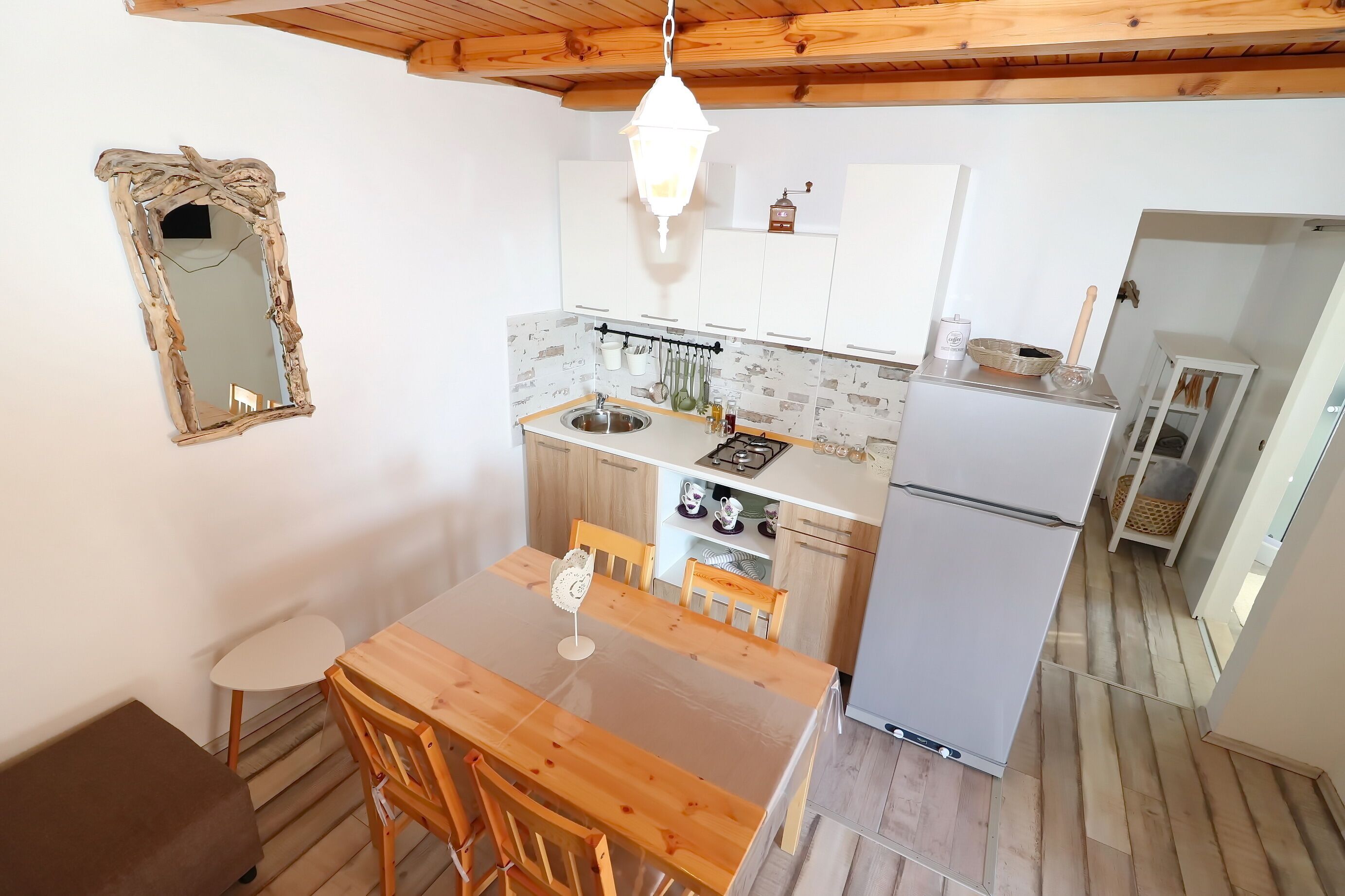 A compact kitchen with a wooden table and chairs, a hanging light fixture, and a white refrigerator.