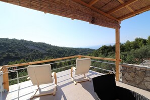 A balcony with two white chairs and a table, overlooking a forested landscape with a clear sky.