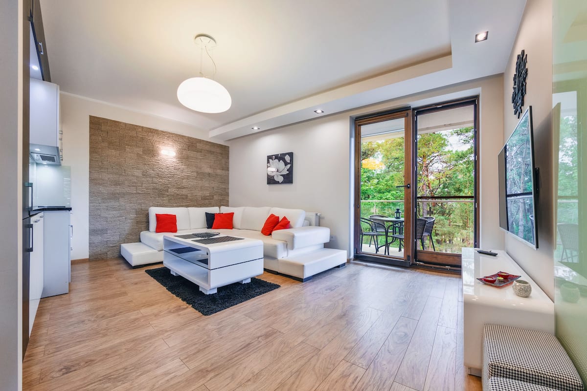 Ein modernes Wohnzimmer mit einem weißen Sofa, einem Couchtisch und einem großen Fenster mit Blick auf Grünflächen.