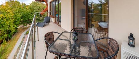A balcony with a glass table and chairs, a small lantern, and a view of trees and a building.
