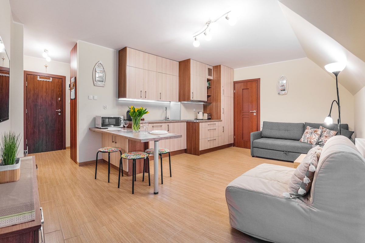 Ein kompakter Wohnraum mit Küchenzeile, Essbereich und einer Sitzecke mit Sofa und Lampe.