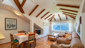 Uma sala de jantar com mesa posta para quatro pessoas, um sofá e vista para o mar através de grandes janelas.