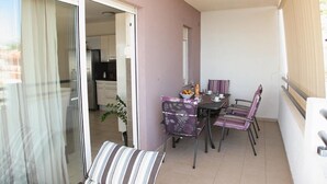 Un balcon avec une table et des chaises, une porte-fenêtre coulissante donnant sur la cuisine et une plante en pot.