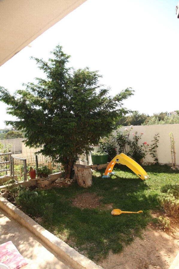 Un pati amb un arbre, un tobogan groc i una zona de jardí.