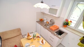 Cocina compacta con una mesa de comedor lista para el desayuno, un lavamanos pequeño y una ventana con flores.