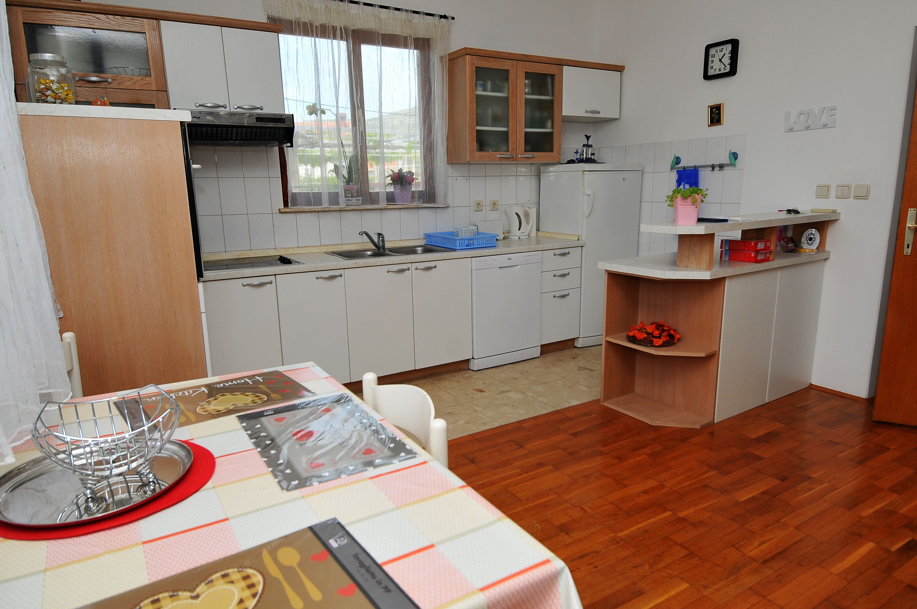 Uma cozinha compacta com armários brancos, bancada de madeira e uma janela com cortinas.