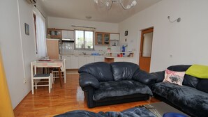 Un salon avec un canapé en cuir noir, une table à manger avec des chaises, et une cuisine en arrière-plan.