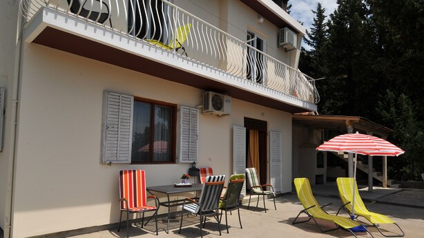 Un bâtiment à deux étages doté d’un balcon, d’un espace extérieur aménagé pour s’asseoir et d’un parasol.