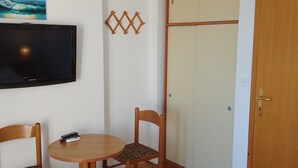 Une chambre comprenant un lit, un téléviseur fixé au mur, deux chaises en bois, une petite table ronde et une armoire.