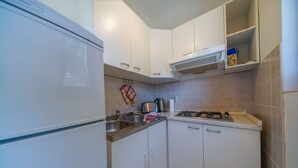 Een kleine keuken met witte kastjes, een gasfornuis, een spoelbak en een inbouwafzuigkap.