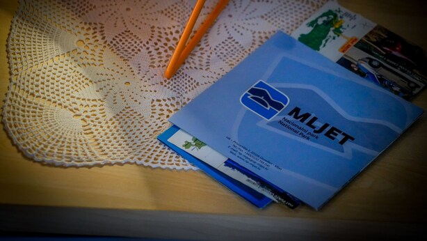Un folleto azul con el título 'MJET National Park' sobre una superficie de madera con un encaje y palillos naranjas.