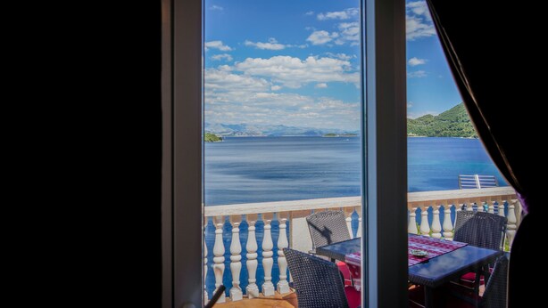 Een balkon met uitzicht op zee en verre eilanden, voorzien van rieten meubels en een tafel met een rode tafelkleed.