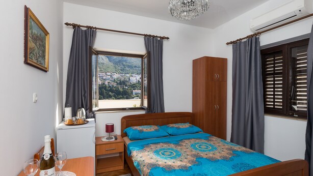 Ein Schlafzimmer mit einem Bett, einem Nachttisch, einem Tisch mit Flasche und Gläsern, einem Kleiderschrank und einem Fenster mit Vorhängen.