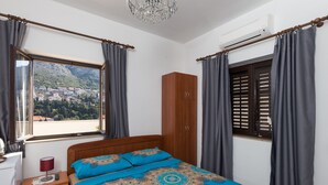 Ein Schlafzimmer mit Bett, Schrank, Nachttisch, Lampe und einem Fenster mit Vorhängen.
