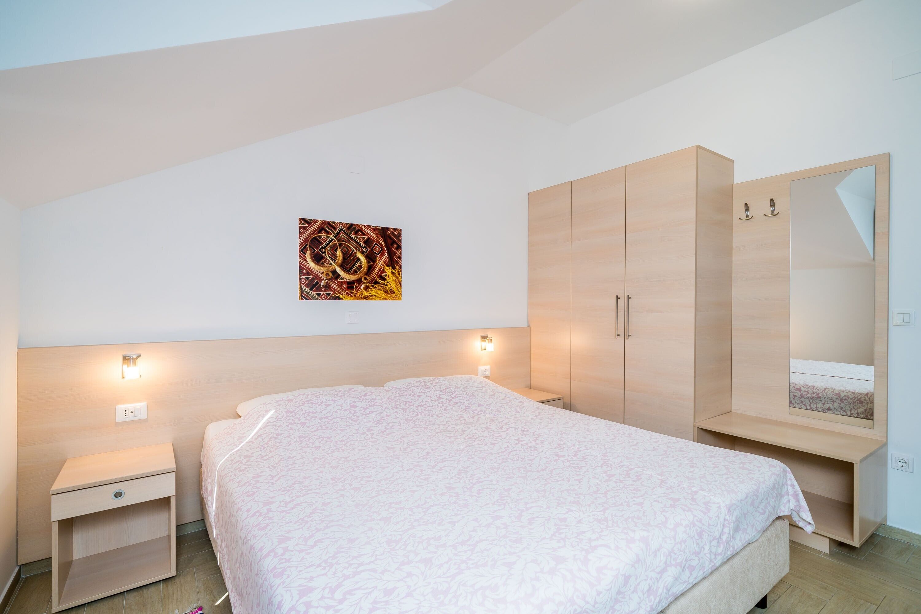 Un dormitorio con cama, mesita de noche, armario y una obra de arte colgada en la pared.