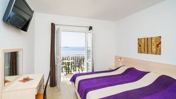 Ein Hotelzimmer mit Bett, Schreibtisch, Stuhl, Fernseher, einem Balkon mit Tisch und Stühlen sowie einem Bild an der Wand.