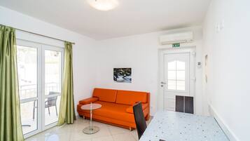 Una stanza con soffitto bianco, una porta bianca con segnale di uscita, un divano arancione, un tavolino rotondo e una sedia.