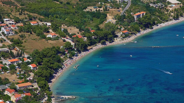 Vue aérienne d’une zone côtière avec une plage, des maisons et des bateaux.
