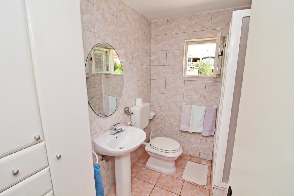 Une salle de bain avec un lavabo, des toilettes et un miroir. Il y a une fenêtre au-dessus des toilettes et un porte-serviettes avec des serviettes.