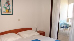 Ein Schlafzimmer mit einem Bett, weißen Kissen, einer blauen Bettdecke, einem Nachttisch mit Lampe und einem gerahmten Bild an der Wand.