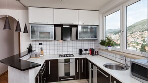Une cuisine moderne avec des armoires blanches, des appareils en acier inoxydable et une grande fenêtre donnant sur la ville.