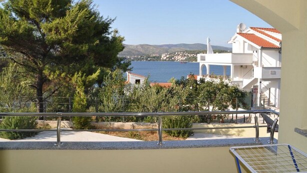 A coastal view with a tree, a white building with a red roof, and a clear blue sea. - Apartments Villa Moonlight - Two Bedroom Apartment with Sea View Terrace (Okrug Gornji)